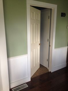 an open door in a green room with white trim on the walls and wood floors