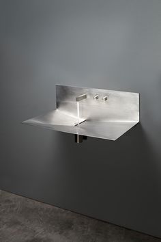 a stainless steel sink mounted to the side of a gray wall in a room with concrete flooring