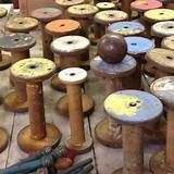 many spools of thread sitting on top of wooden poles in a room filled with other spools