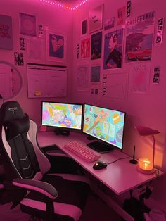 two computer monitors sitting on top of a desk in front of a pink wall covered with posters