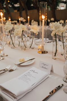 the table is set with silverware and white flowers in vases, candles and menu cards