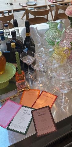 there are many wine glasses on the table with cards in front of them and bottles behind it