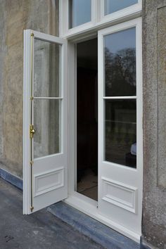 an open window on the side of a building with white trim and gold hardware, in front of a stone wall