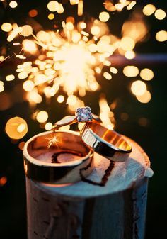 two wedding rings sitting on top of a wooden barrel with fireworks in the sky behind them