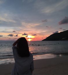 a woman standing on top of a sandy beach next to the ocean at sun set