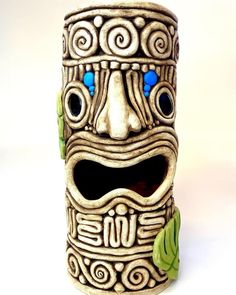 a ceramic tiki mask with blue eyes and green leaves