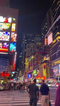 two men walking across a street in front of tall buildings with neon signs on them