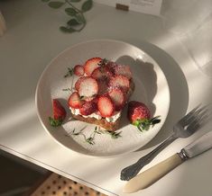 a plate with strawberries on it next to a fork and knife