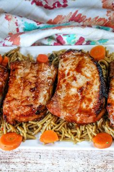 some meat and noodles on a plate with carrots, broccoli and sauce