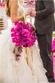 a man and woman standing next to each other in front of a purple flower bouquet