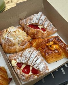 four pastries in a box with strawberries and almonds on the top one is filled with powdered sugar