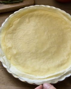 a person holding a pie crust in front of an uncooked pie dish on a wooden table