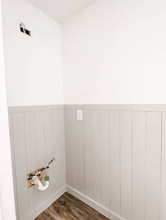 an empty bathroom with white walls and wood flooring on the wall, along with a toilet paper dispenser