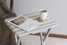 a cup of coffee sits on top of a small table with a book and magazine