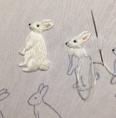 two white rabbits on a light blue background with some thread in the foreground and one bunny holding a stick