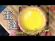 a person holding a yellow egg tart on top of a wooden cutting board with chinese writing