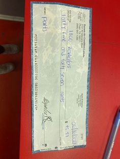 a chequed check for $ 1, 000 is on a red table next to a pen