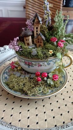 a teacup filled with moss and little houses on top of it's saucer