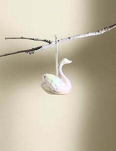 a white swan ornament hanging from a twig on a branch with no leaves