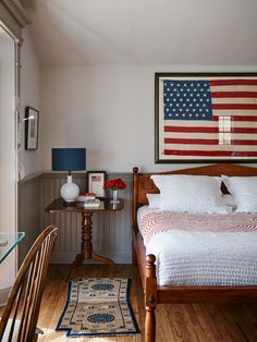 an american flag is hanging above a bed in a bedroom with wood floors and white walls