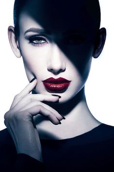 a woman with dark makeup and red lipstick posing for the camera, her hand on her chin