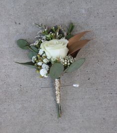 a boutonniere with white flowers and greenery on the ground in front of a wall