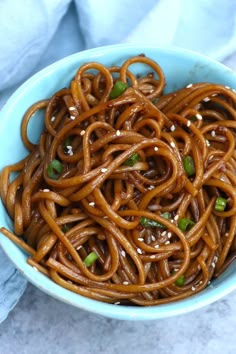 a blue bowl filled with noodles on top of a white table cloth next to chopsticks