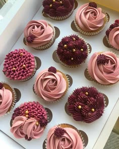 twelve cupcakes with pink frosting and purple flowers on them in a box