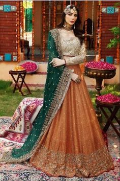 a woman in an orange and green lehenga standing on a rug with flowers