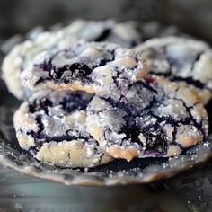 two blueberry crinkle cookies sitting on top of a glass plate covered in powdered sugar