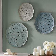 three decorative plates hanging on the wall above a table with candles and flowers in vases