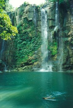 there is a large waterfall in the middle of this body of water with people swimming below it