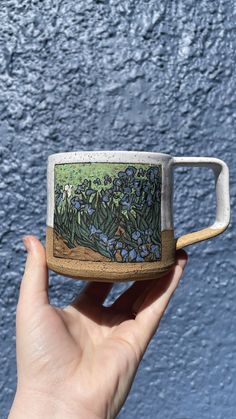 a hand holding a ceramic mug with blue flowers on the outside and green leaves on the inside