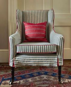 a striped chair sitting on top of a rug in front of a wall with a red pillow