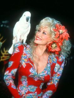 a woman holding a white parrot on her shoulder and wearing a flower in her hair