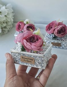 a hand holding a small silver box with pink flowers in it