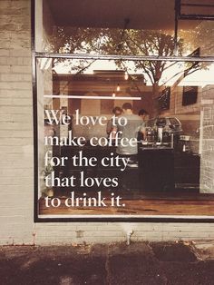 the reflection of two people standing in a coffee shop's window that says, we love to make coffee for the city that loves to drink it