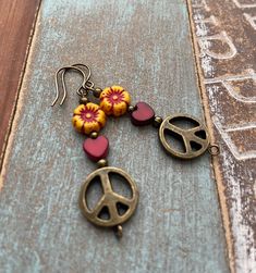 Peace, love, and earrings! You will love these beautiful floral earrings! They are handmade with brass peace sign beads, Czech glass flower beads, and jasper stone hearts. A perfect addition to your jewelry collection! Product Details: *Copper Ear wires *Lightweight, perfect for everyday wear *Handmade glass, brass, and stone beads *A perfect gift for the jewelry lover in your life **To view more of my original jewelry designs, please visit my Etsy shop at: rabbiteardesigns.Etsy.com or follow me Hippie Jewelry With Dangling Beads For Gift, Hippie Beaded Earrings Gift, Hippie Beaded Dangle Earrings, Boho Earrings Hippie Bohemian, Vintage Jewelry With Peace Sign As Gift, Vintage Jewelry With Peace Sign For Gift, Peace Sign Earrings Boho, Wooden Peace Sign Ear Rings, Diy Earrings Dangle