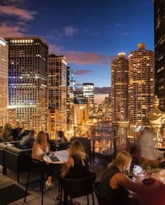 people are sitting at tables on the roof of a high rise building with city lights in the background