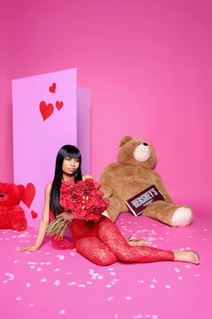 a woman sitting on the ground next to a teddy bear and holding flowers in her hands