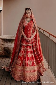 a woman in a red and gold bridal gown standing on a wooden floor next to a wall