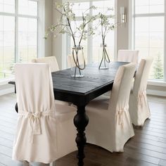 a dining room table with white chairs and flowers in vases