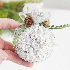 a hand holding a white ornament with pine cones and pearls on the top