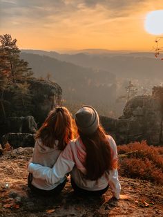 two people sitting on top of a mountain looking at the sunset