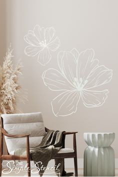 a chair and vase in front of a wall with flowers on it