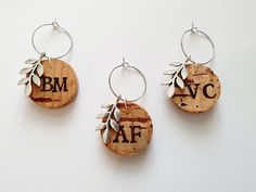 three wine cork earrings with leaves and letters on them, hanging from silver hoop holders