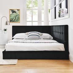 a bed with white sheets and black headboard in a room next to a window