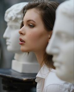 a woman standing in front of several white busturines with their heads turned to the side