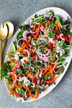 a white plate topped with a salad next to a golden spoon and fork on top of a gray surface