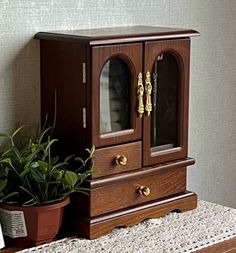 a small wooden cabinet sitting on top of a table next to a potted plant